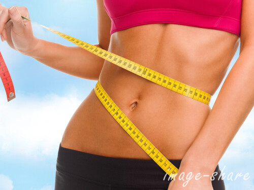 sport, fitness and diet concept - close up of trained belly with measuring tape